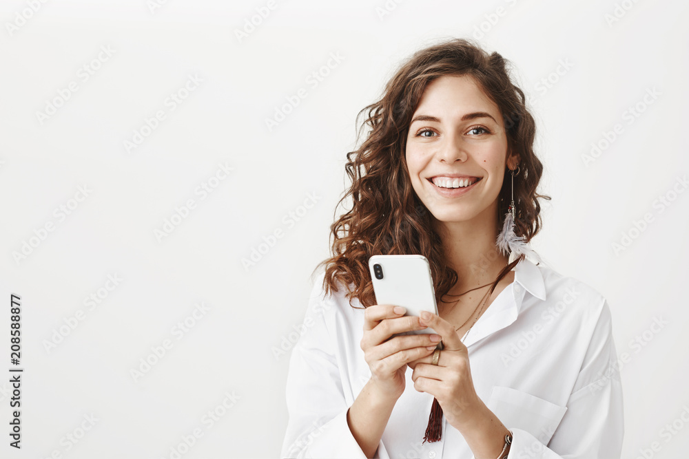 Portrait of happy feminine caucasian woman holding smartphone with both hands, smiling and looking joyfully at camera while standing against gray background. Mom wrote that she reached destination Portrait of happy feminine caucasian woman holding smartphone with both hands, smiling and looking joyfully at camera while standing against gray background. Mom wrote that she reached destination
