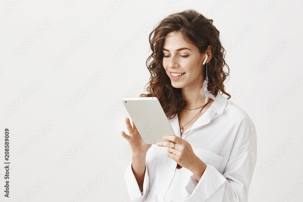 Portrait of sexy confident caucasian woman with stylish haircut browsing in tablet with broad smile and expressing positive emotions, standing against gray background. Girl looks in her timetable Portrait of sexy confident caucasian woman with stylish haircut browsing in tablet with broad smile and expressing positive emotions, standing against gray background. Girl looks in her timetable