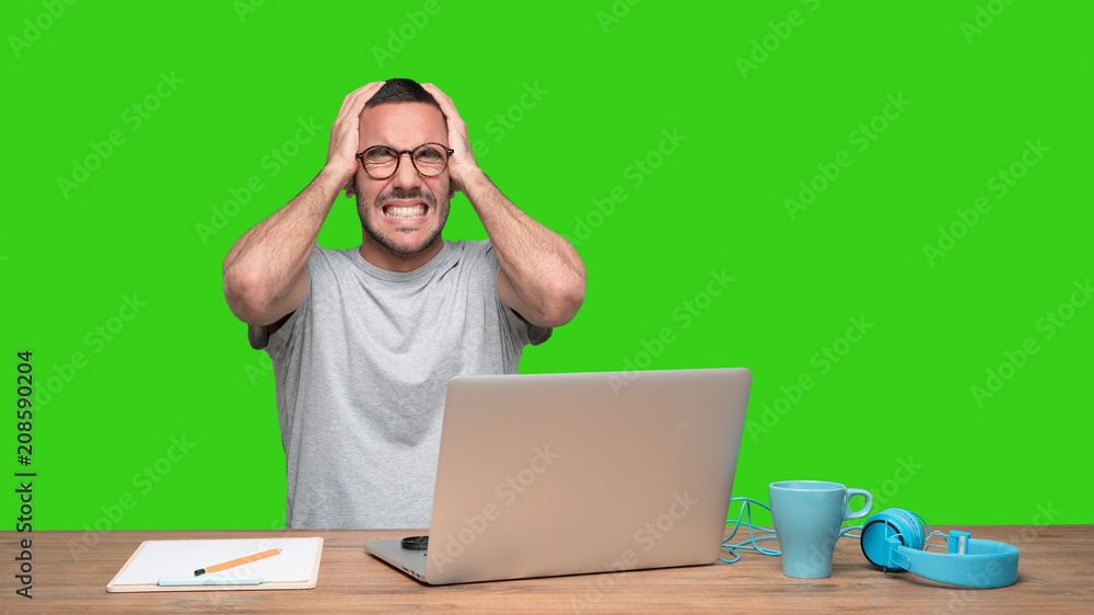 Concerned young man sitting at his desk - Green background Concerned young man sitting at his desk - Green background