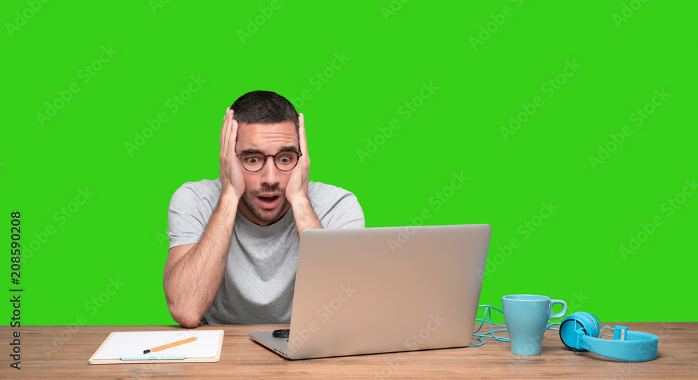 Concerned young man sitting at his desk - Green background Concerned young man sitting at his desk - Green background