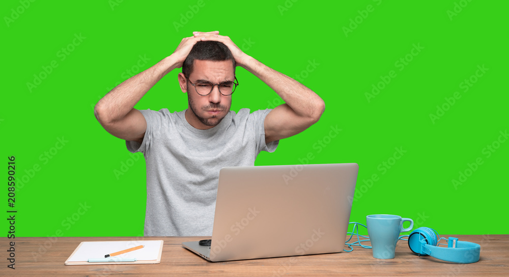 Concerned young man sitting at his desk - Green background Concerned young man sitting at his desk - Green background