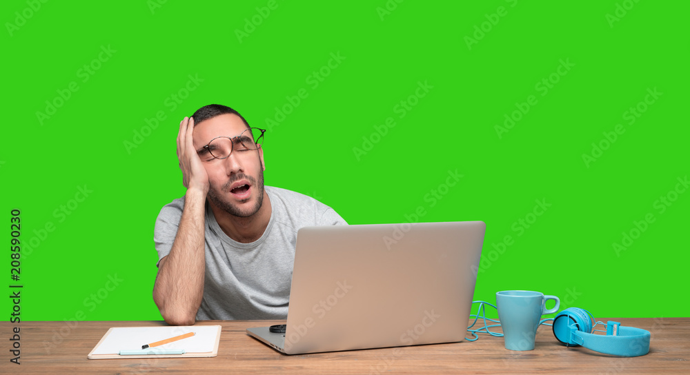 Tired young man sitting at his desk - Green background Tired young man sitting at his desk - Green background