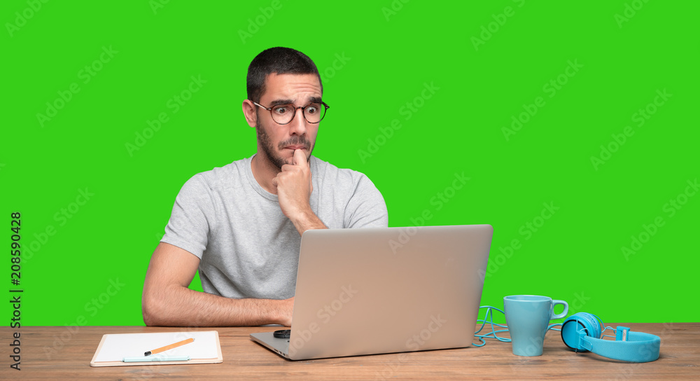 Astonished young man sitting at his desk - Green background Astonished young man sitting at his desk - Green background