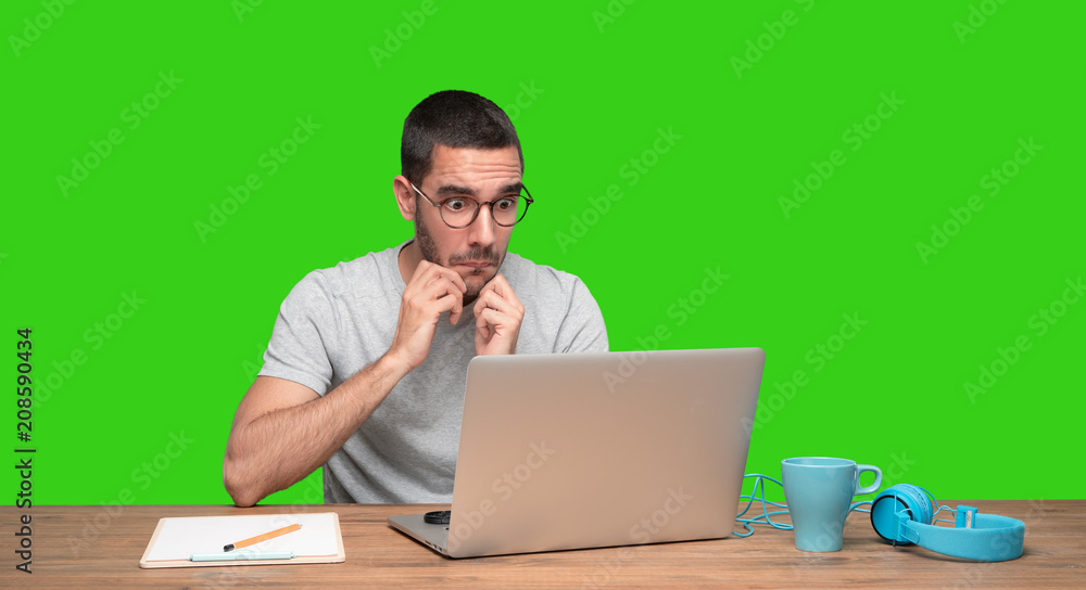 Astonished young man sitting at his desk - Green background Astonished young man sitting at his desk - Green background