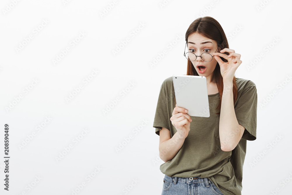 Portrait of surprised overwhelmed attractive woman in round glasses, holding hand on rim and dropping jaw while seeing photo of boyfriend with some girl, holding digital tablet shocked and amazed Portrait of surprised overwhelmed attractive woman in round glasses, holding hand on rim and dropping jaw while seeing photo of boyfriend with some girl, holding digital tablet shocked and amazed