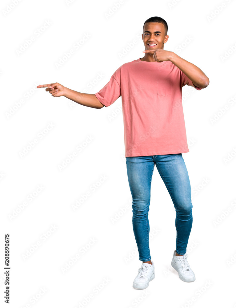 Standing young african american man pointing finger to the side and presenting a product while smiling on isolated white background Standing young african american man pointing finger to the side and presenting a product while smiling on isolated white background