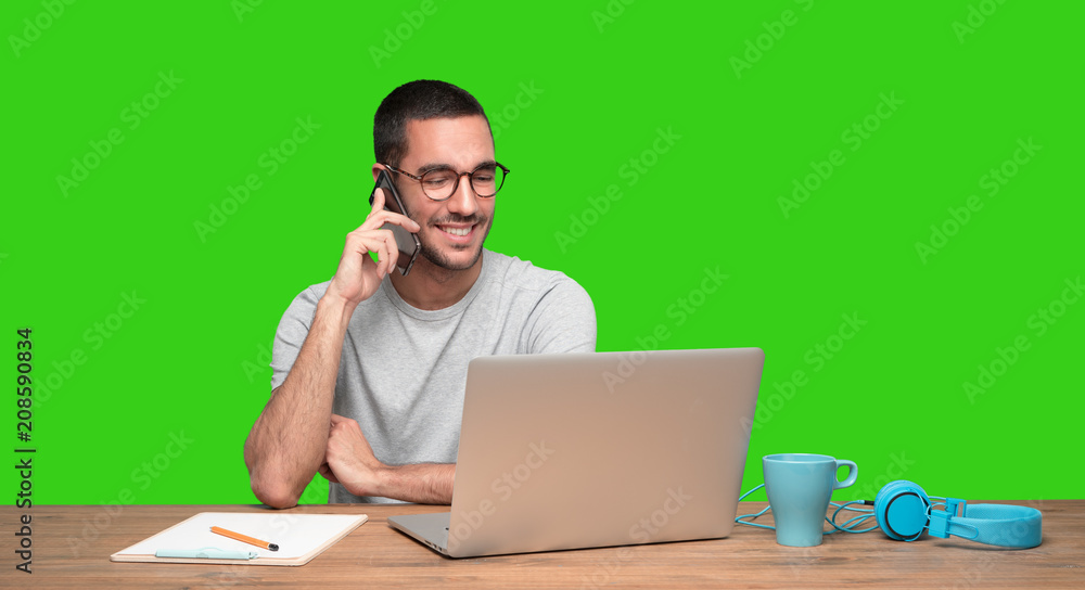 Happy young man on the phone and sitting at his desk - Green background Happy young man on the phone and sitting at his desk - Green background