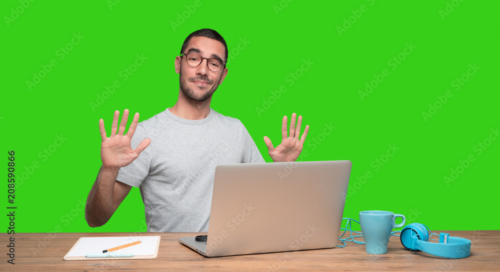 Confident young man sitting at his desk with a keep calm gesture - Green background Confident young man sitting at his desk with a keep calm gesture - Green background