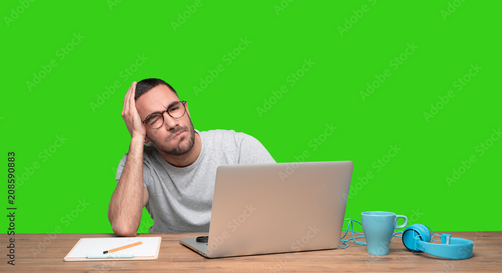Depressed young man sitting at his desk - Green background Depressed young man sitting at his desk - Green background
