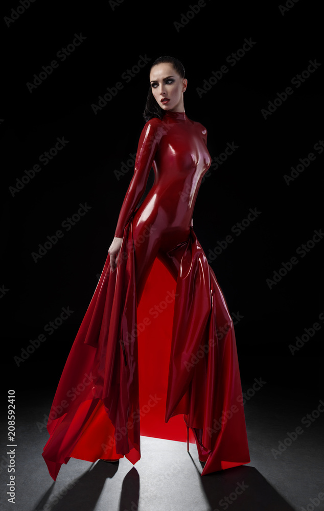 Brunette woman in red latex slim suit posing on dark background