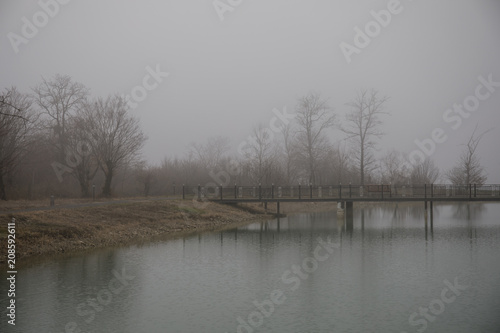 Amazing landscape of bridge reflect on surface water of lake, fog evaporate from pond make romantic scene or Beautiful bridge on lake with trees at fog.