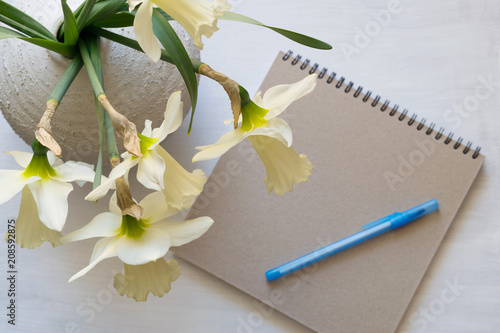 Notepad with pen, daffodils in a vase on a white table. Inspirational workplace.