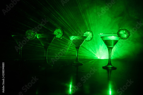 Several glasses of famous cocktail Martini, shot at a bar with dark toned foggy background and disco lights. Club drink concept.
