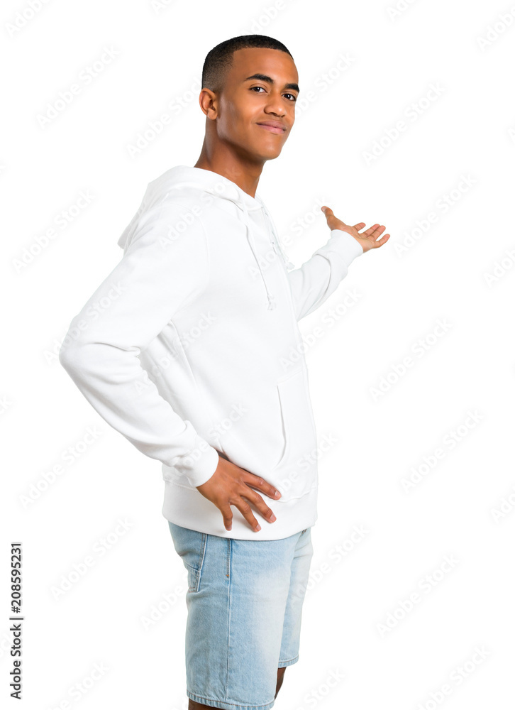 Dark-skinned young man with white sweatshirt pointing back with the index finger presenting a product on isolated white background Dark-skinned young man with white sweatshirt pointing back with the index finger presenting a product on isolated white background