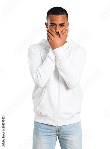 Dark-skinned young man with white sweatshirt covering mouth with both hands for saying something inappropriate. Can not speak on isolated white background © luismolinero