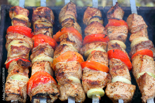 Pieces of juicy slices of marinated pork meat strung on skewers with slices of chopped tomatoes and onion cooking on the grill. Cooking shashlik on the brazier Close-up.
