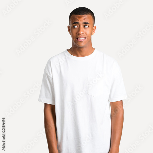 Young african american man is a little bit nervous and scared pressing the teeth on isolated background