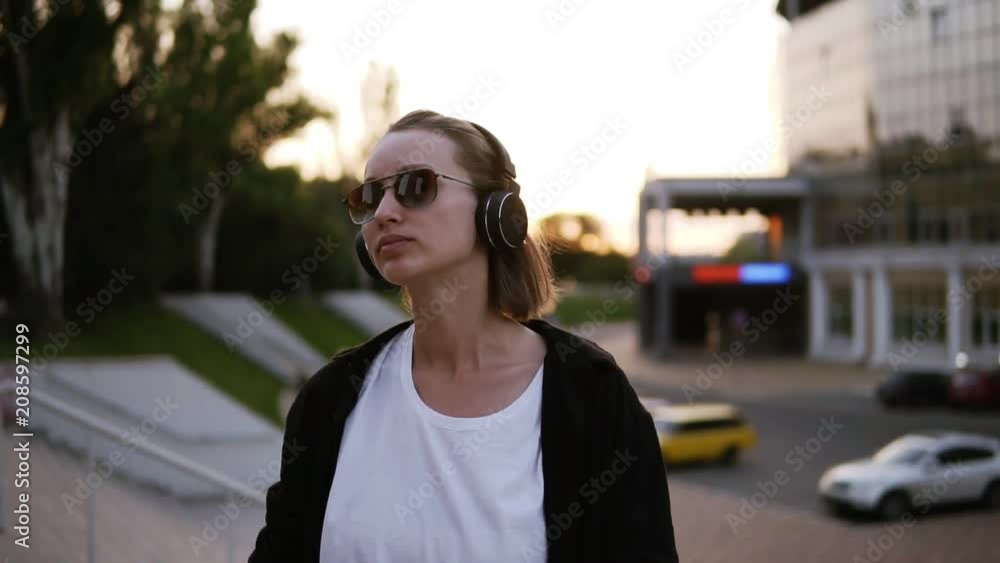 Trendy, attractive girl in stylish youth clothes freely dancing outside on the street. Listening to the music in black headphones, feeling good. Slow motion Trendy, attractive girl in stylish youth clothes freely dancing outside on the street. Listening to the music in black headphones, feeling good. Slow motion