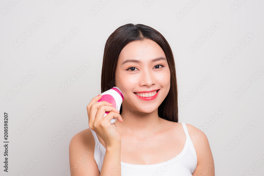 Skin Care. Side portrait of the charming healthy fresh woman with natural make-up using the electric facial massager at isolated white background. Skin Care. Side portrait of the charming healthy fresh woman with natural make-up using the electric facial massager at isolated white background.