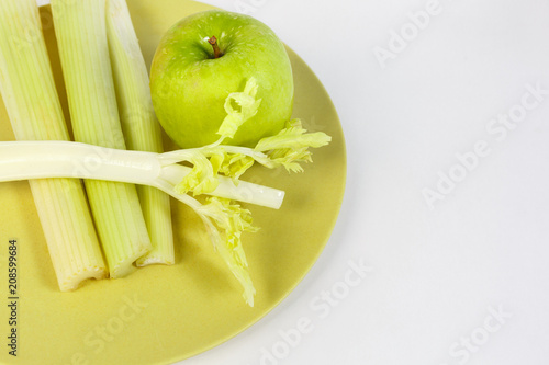 all for fresh juice: fresh celery and green Apple on a plate of mustard color on a white background