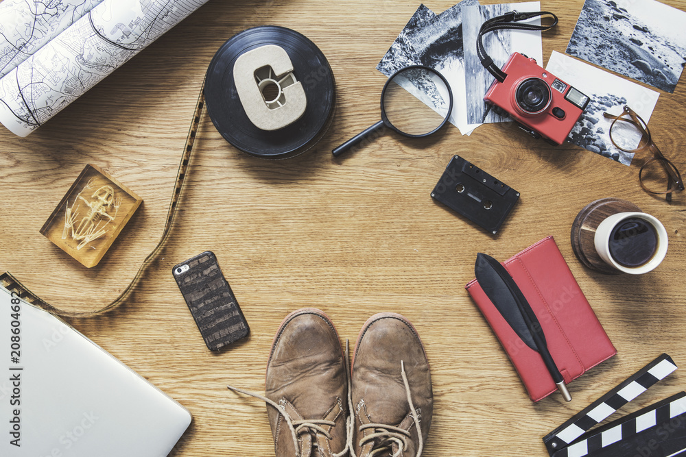 Stylish composition of flat lay on wooden desk with laptop, photo plate, map, cup of coffee, phone, shoes notebook, camera and office accessories. Creative desk of traveler, photographer. Stylish composition of flat lay on wooden desk with laptop, photo plate, map, cup of coffee, phone, shoes notebook, camera and office accessories. Creative desk of traveler, photographer.