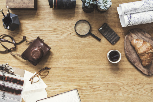 Stylish composition of flat lay on wooden desk with succulent, map, cup of coffee, croissant, phone, notebook, camera and office accessories. Creative desk of freelancer. Copy space for inscription.