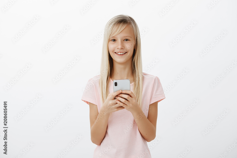 Adorable positive child feeling great finally talk with father who works abroad. Satisfied cheerful cute blond girl in pink t-shirt, holding expensive smartphone and smiling broadly at camera Adorable positive child feeling great finally talk with father who works abroad. Satisfied cheerful cute blond girl in pink t-shirt, holding expensive smartphone and smiling broadly at camera