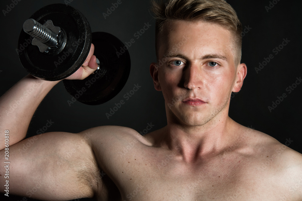 Gym and dumbbells. Young attractive guy. Black background. 