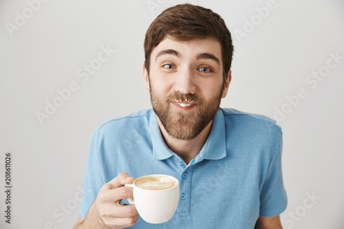 You have something on your moustache. Portrait of funny playful bearded guy drinking cup of cappuccino and having milk on face, smiling and being carefree while sitting in cafe with girlfriend