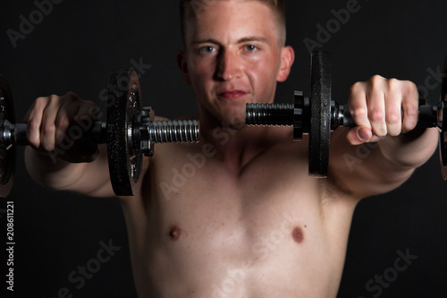 Gym and dumbbells. Young attractive guy. Black background. 