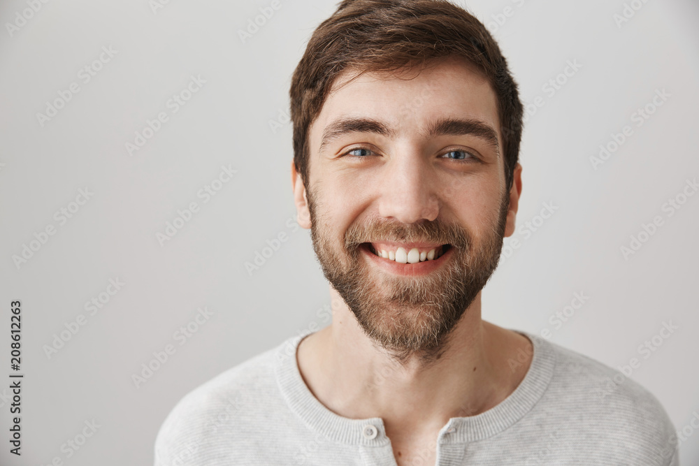 Close-up portrait of friendly kind european guy smiling broadly as if assuring that he always ready to help, standing over gray background. Pleasant neighbour talks with friends on porch Close-up portrait of friendly kind european guy smiling broadly as if assuring that he always ready to help, standing over gray background. Pleasant neighbour talks with friends on porch