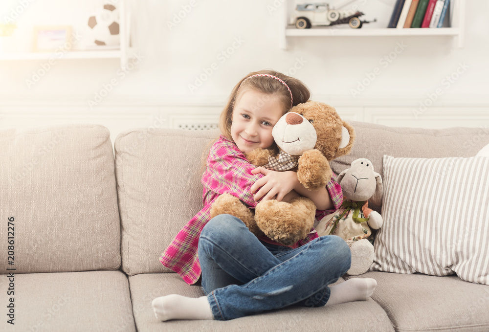 Happy little hugging her teddy bear on sofa