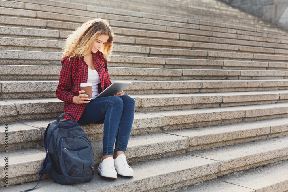 Female student working on a laptop and drinking coffee outside Female student working on a laptop and drinking coffee outside