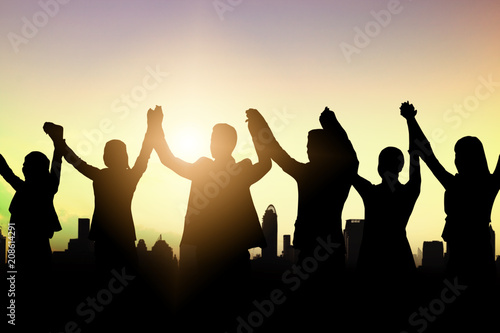 silhouette of business people team and successful teamwork celebration and happiness staning on top of boulding in summer sunset