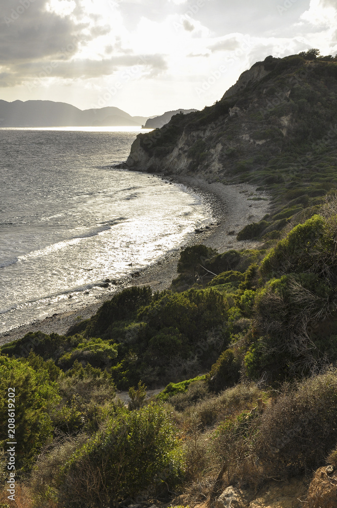 Landscape of romantic summer evening by the sea. Seascape of small waves on sea, empty sand beach, hills with green dune vegetation and mountains on horizon.