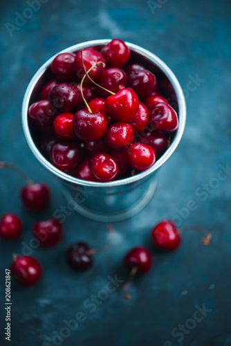 Cherries with a small metal bucket on a grey concrete background, summer berries concept with copy space. Neutral color tones still life