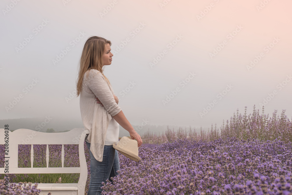 Beautiful young woman holding a hat is on the lavender field