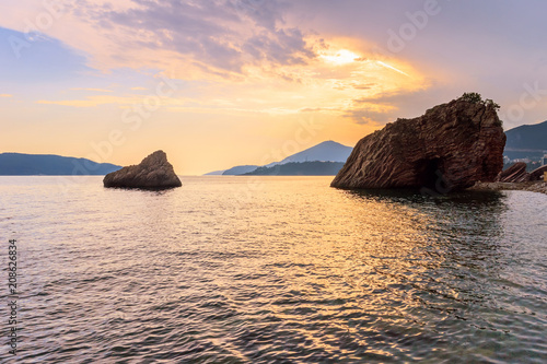 Golden sunset on Adriatic sea with reflections and big stones in the water, Montenegro