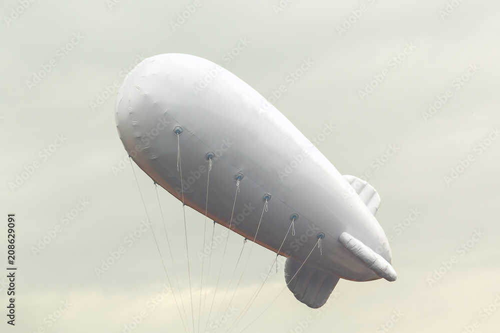 Fototapeta premium White inflatable dirigible with a place for a logo on a background of a gray sky with clouds