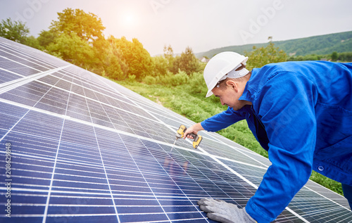 Construction worker connects photo voltaic panel to solar system using screwdriver. Professional installing and construction of solar system, alternative energy and financial investment concept.