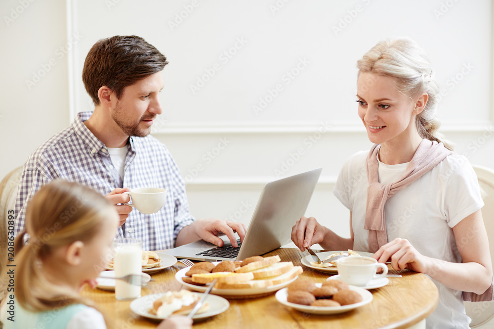 Young mother and little girl eating breakfast while businessman networking near by