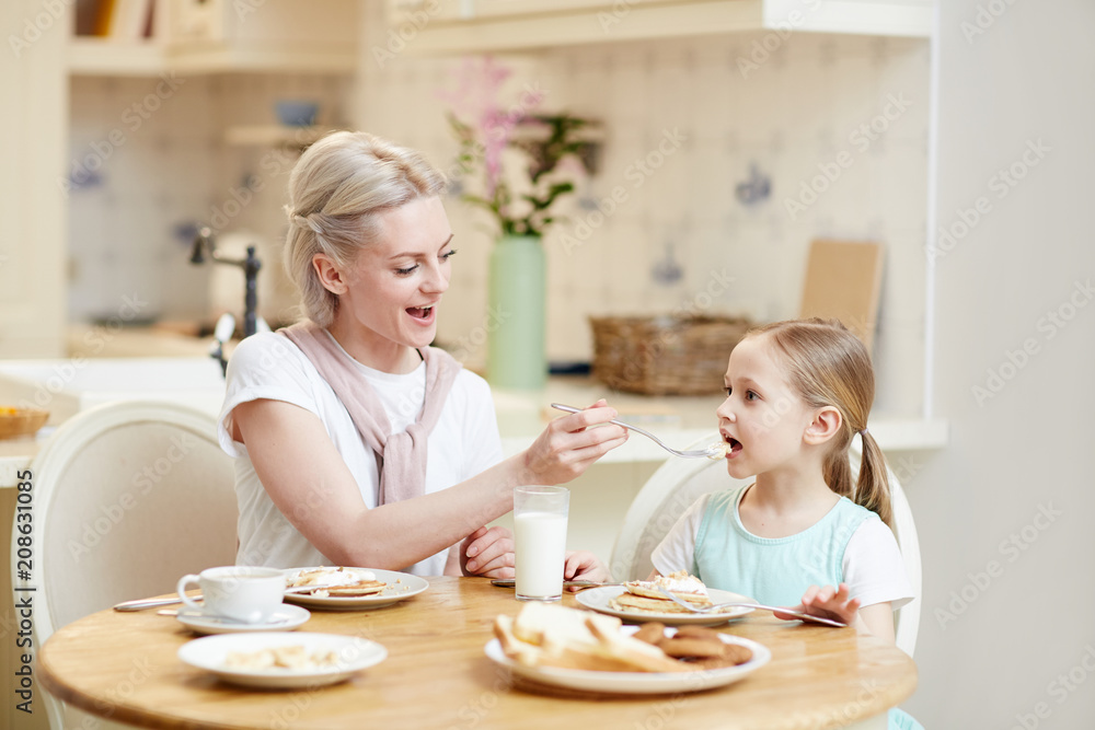 Young woman feeding her daughter with homemade food by breakfast Young woman feeding her daughter with homemade food by breakfast