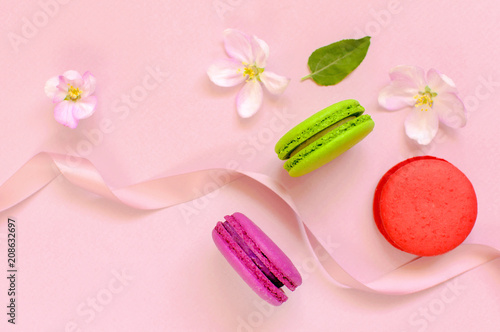 Cake macaron or macaroon with pink gift ribbon spring flowers on pink background top view flat lay  beautiful dessert  colorful almond cookies  pastel colors