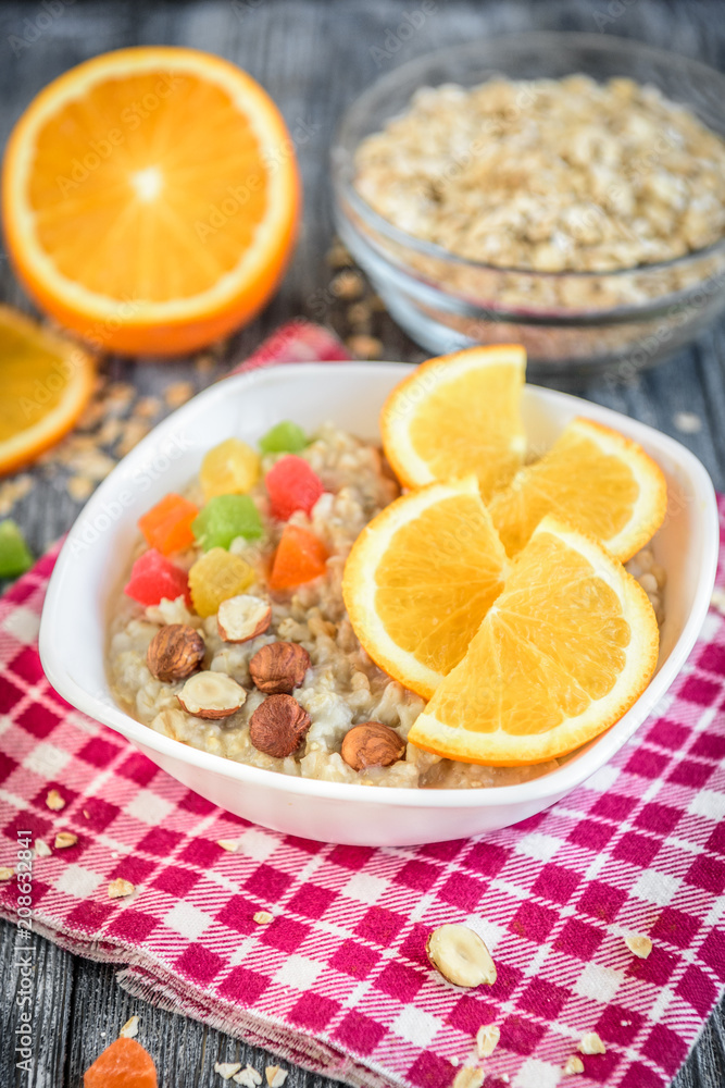 Homemade oatmeal porridge with orange, candied fruit and hazelnut on grey wooden background. Healthy breakfast. Homemade oatmeal porridge with orange, candied fruit and hazelnut on grey wooden background. Healthy breakfast.