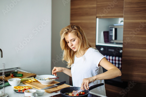 Blonde housewife of caucasian appearence preparing turkey kebabs on frying pan over the kitchen photo