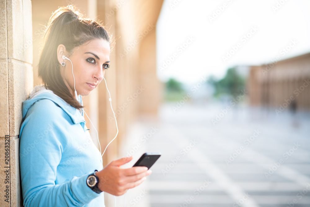 sports lady outdoors listening music with earphones using mobile phone