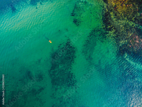 Looking down at shallow turquoise transparent ocean water and small yellow fishing boat
