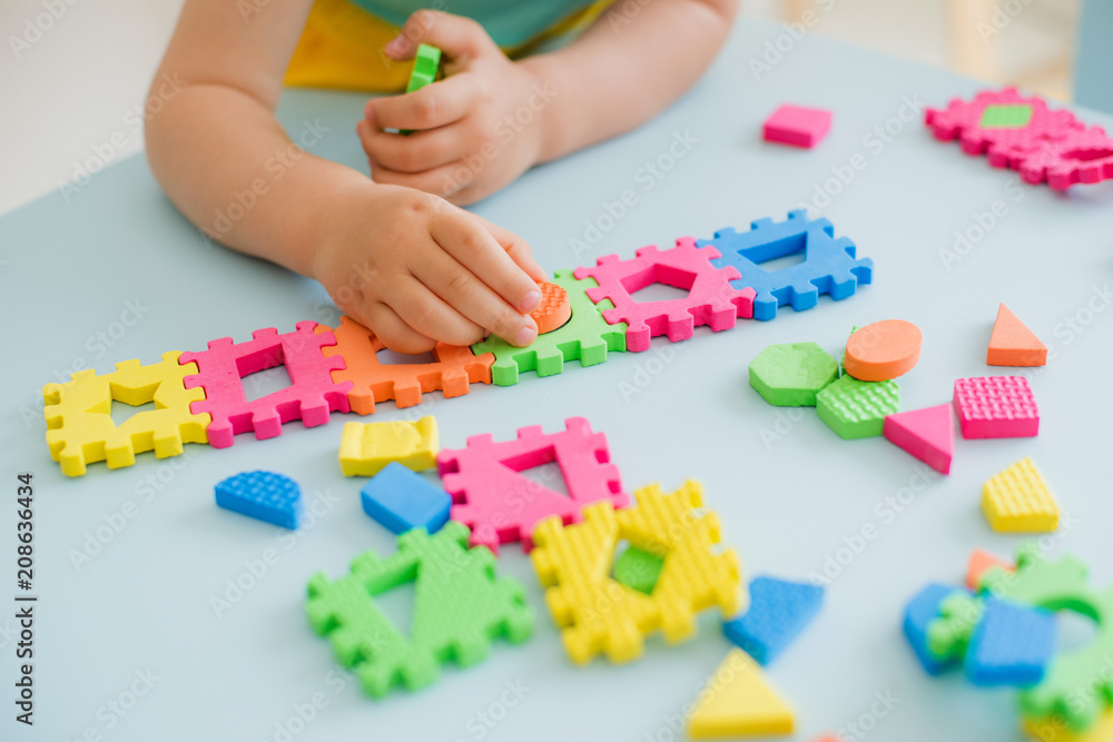 little girl playing at a children's table with a puzzle, early education. Bright soft blocks little girl playing at a children's table with a puzzle, early education. Bright soft blocks
