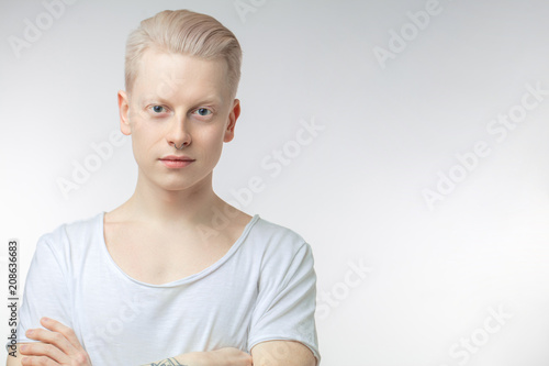 Portrait of blonde young man with uncommon appearance wears white t shirt, looking at camera, isolated over white studio background with copyspace for text.