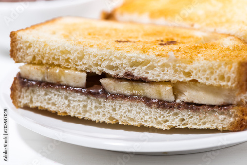 sweet sandwich with chocolate paste and banana on white table, closeup